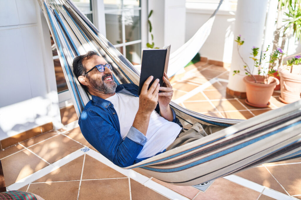 Man relaxing in a hammock and reading a book on a sunny patio
